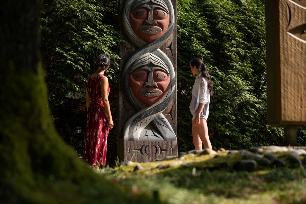 A couple are looking at the Stanley Park Totems.